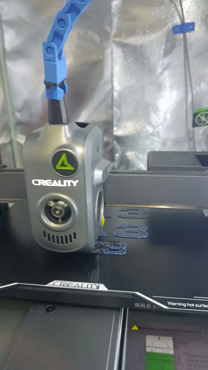 Close-up of a Creality toolhead drawing the first layers of a blue A3 car badge onto the build plate