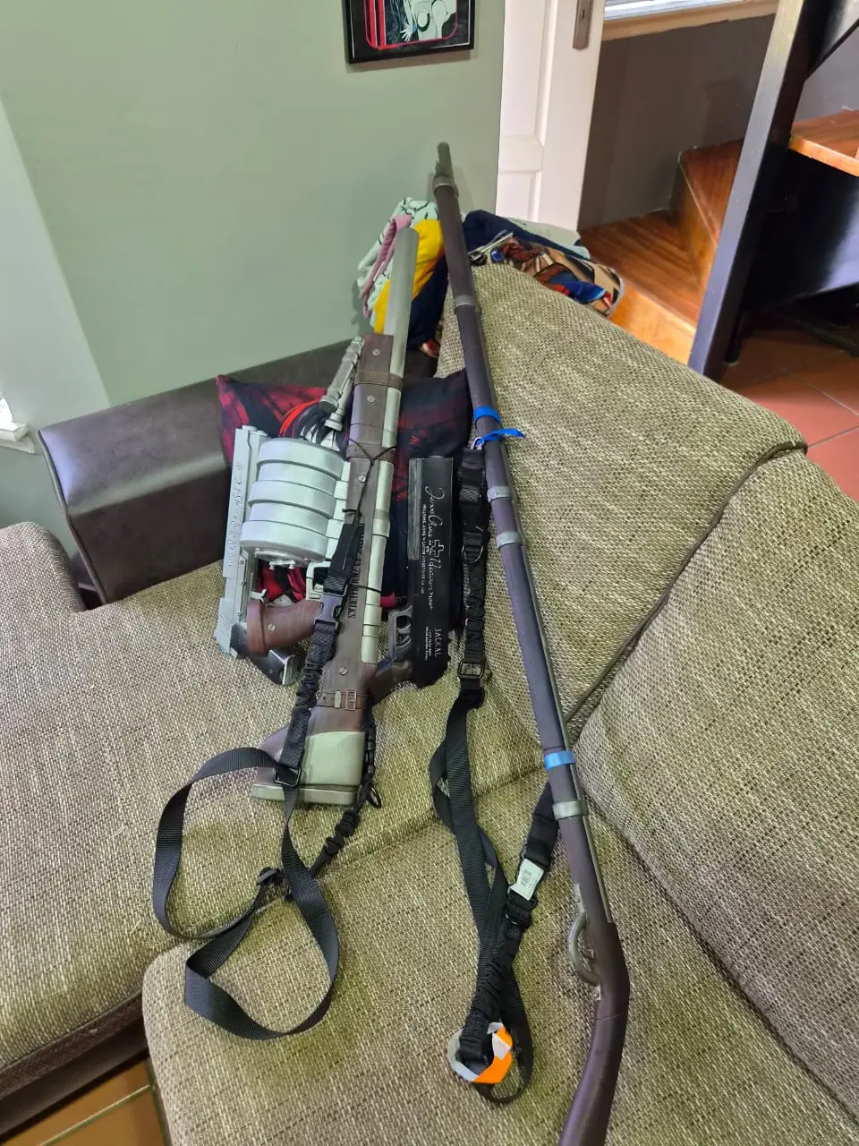 The full Hellsing prop set on a couch: the Harkonnen cannon with its drum magazine, both pistols, and Rip Van Winkle's long musket