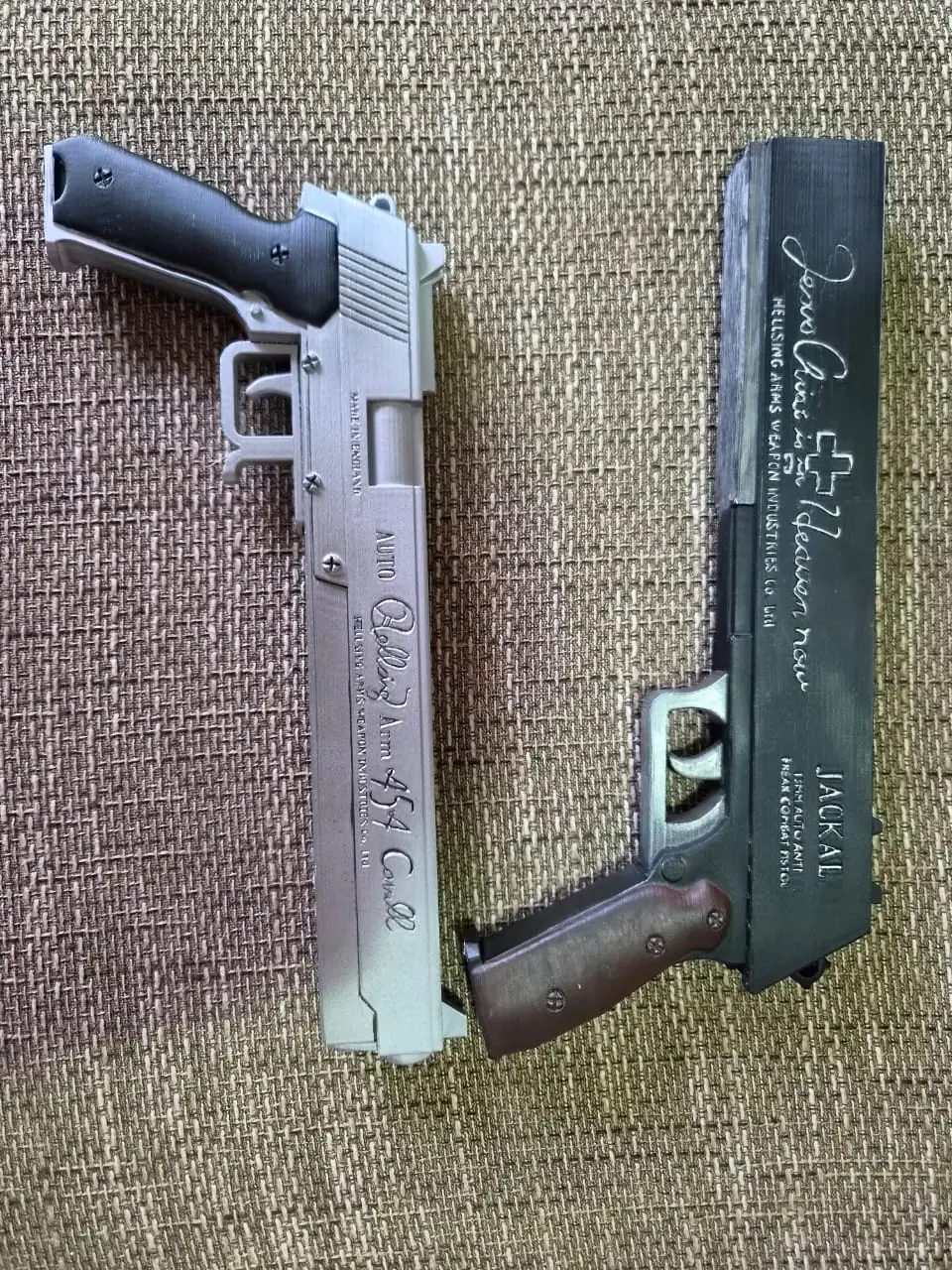 Alucard's silver 454 Casull and black Jackal pistols side by side, showing the raised engraved lettering on both slides