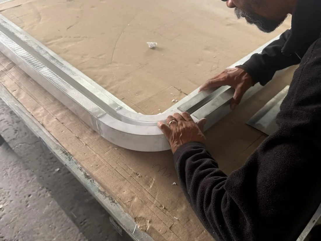 A printed corner being fitted between two straight aluminium extrusion sections on the workbench, forming the radiused corner of the ceiling light frame
